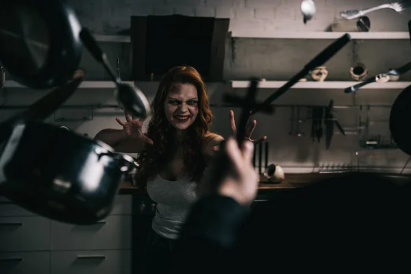 Selective focus of demon with levitating cookware and exorcist with cross in kitchen — Stock Photo