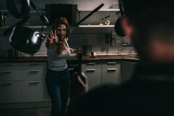 Selective focus of female demon with levitating cookware and exorcist with cross in kitchen — Stock Photo