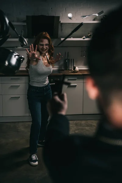 Вибірковий фокус моторошної демонічної дівчини з висвітлюючим посудом і екзорцистом з хрестом на кухні — стокове фото