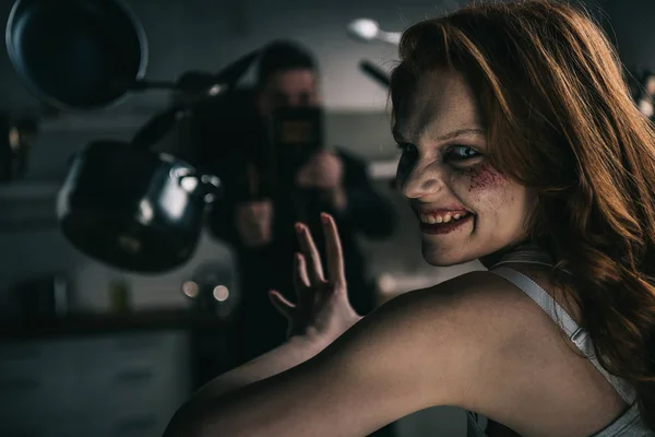 Selective focus of exorcist and smiling demon with levitating cookware in kitchen — Stock Photo