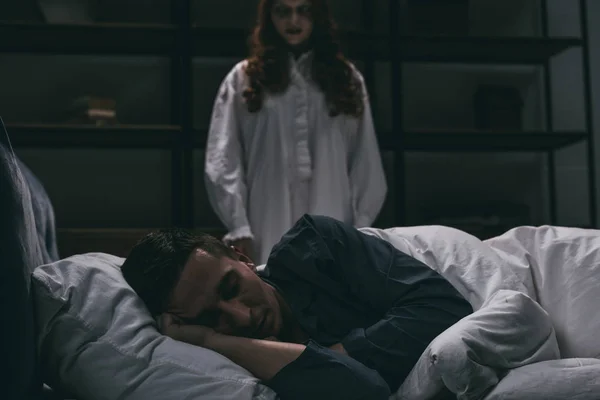 Donna ossessionata in piedi vicino al letto con l'uomo addormentato — Foto stock