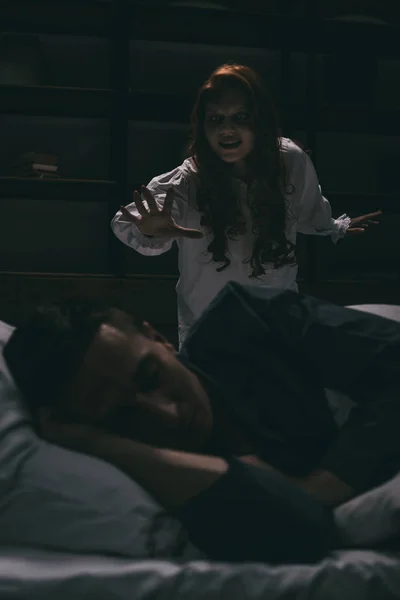Демонічна усміхнена жінка стоїть над сплячим чоловіком у спальні — стокове фото