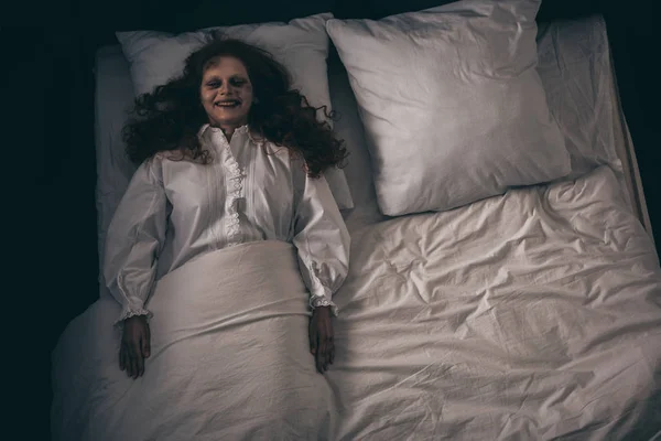 Top view of creepy smiling demon in nightgown lying in bed — Stock Photo