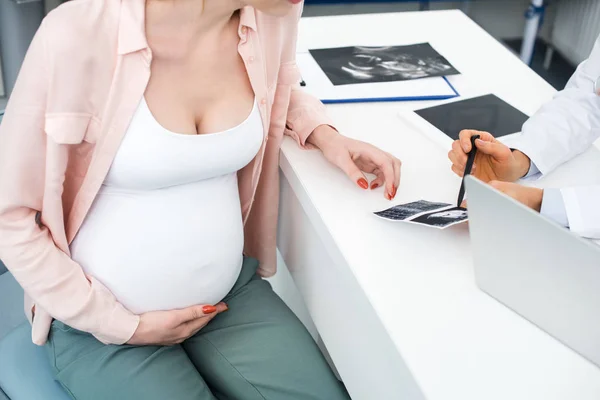 Vista recortada del médico que muestra una ecografía a una mujer embarazada joven en la clínica - foto de stock