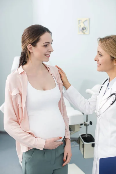 Улыбающаяся беременная женщина консультируется с врачом в гинекологической клинике — стоковое фото