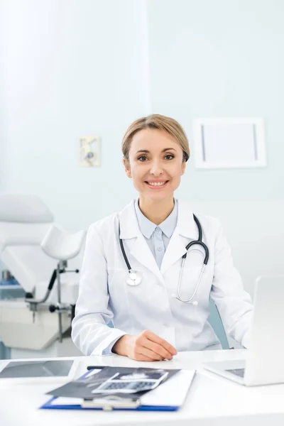 Médico sonriente profesional con computadora portátil y ecografías en la clínica - foto de stock