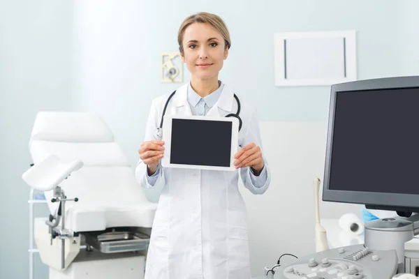 Doctora profesional mostrando tableta digital con pantallas en blanco en clínica con escáner de ultrasonido - foto de stock