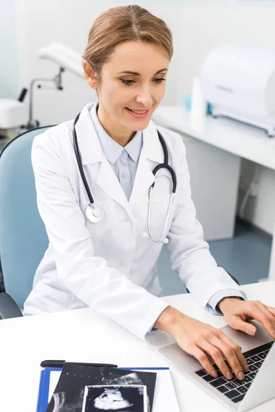 Professional female doctor with ultrasound scans working on laptop in clinic — Stock Photo