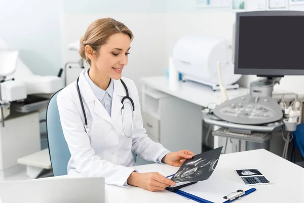 Médico sonriente profesional que mira la ecografía en la clínica - foto de stock