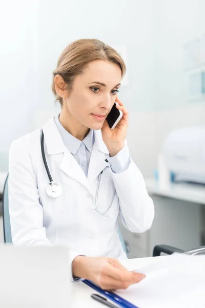 Médico profesional que sostiene hablar en el teléfono inteligente en la clínica - foto de stock