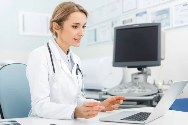 Belle femme médecin travaillant sur ordinateur portable en clinique avec scanner à ultrasons — Photo de stock
