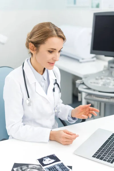 Doctora profesional que trabaja en la computadora portátil en la clínica con ecografías - foto de stock