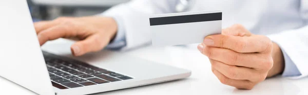 Panoramic shot of doctor using laptop and credit card in clinic — Stock Photo