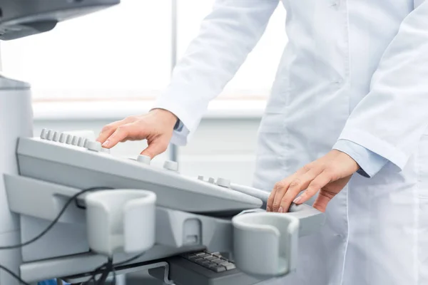 Обрезанный вид врача в белом халате, работающего с ультразвуковым сканером в клинике — стоковое фото