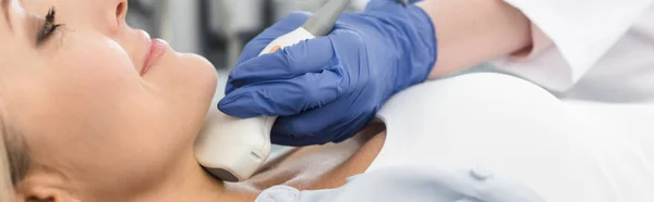 Visão recortada do médico que examina a tireóide do paciente feminino com ultra-som na clínica, tiro panorâmico — Fotografia de Stock