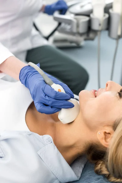 Doctor examining thyroid of smiling woman with ultrasound scan in clinic — Stock Photo