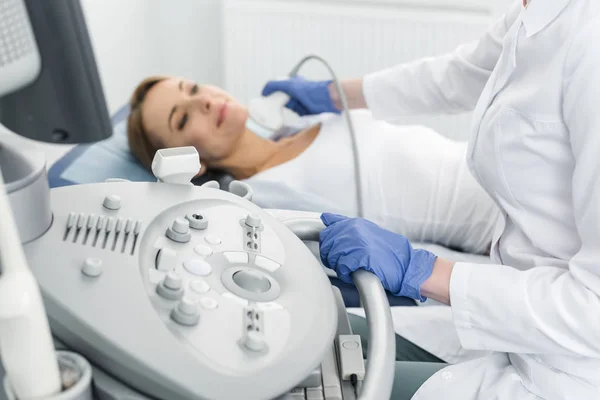 Young doctor examining thyroid of female patient with ultrasound scan in clinic — Stock Photo