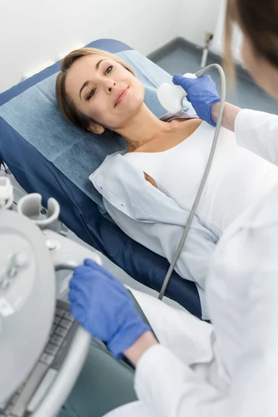 Jeune médecin examinant la thyroïde du patient souriant avec échographie en clinique — Photo de stock