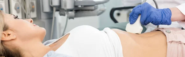Tiro panorâmico do médico examinando o estômago do paciente loiro feminino com ultra-som na clínica — Fotografia de Stock