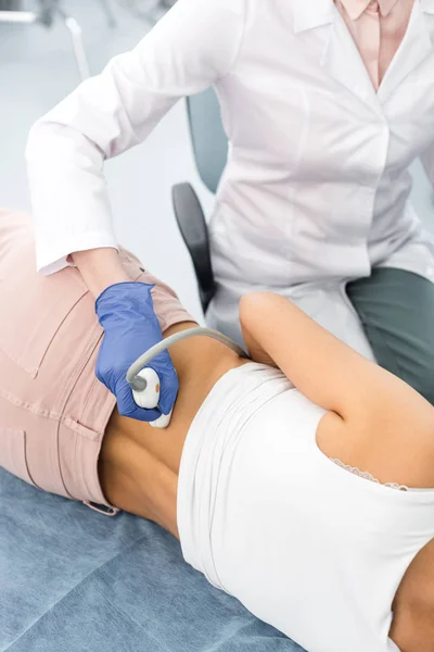 Vista recortada del médico examinando el riñón de la paciente femenina con ecografía en la clínica - foto de stock