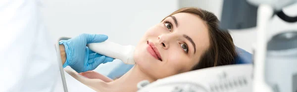 Panoramic shot of doctor examining thyroid of smiling patient with ultrasound scan in clinic — Stock Photo