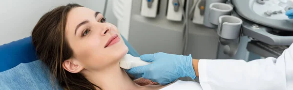 Panoramic shot of professional doctor examining thyroid of female patient with ultrasound scan in clinic — Stock Photo