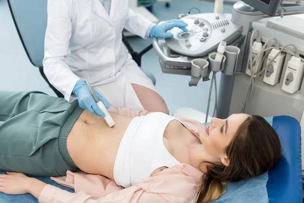 Female doctor examining stomach of patient with ultrasound scan in clinic — Stock Photo