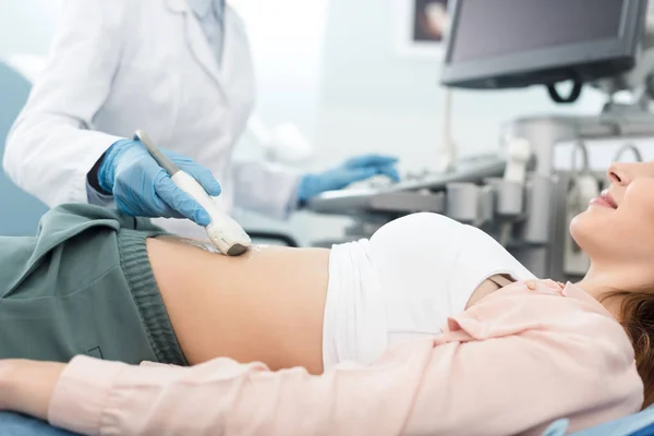 Vista recortada del médico examinando el estómago de la paciente femenina con ecografía en la clínica - foto de stock