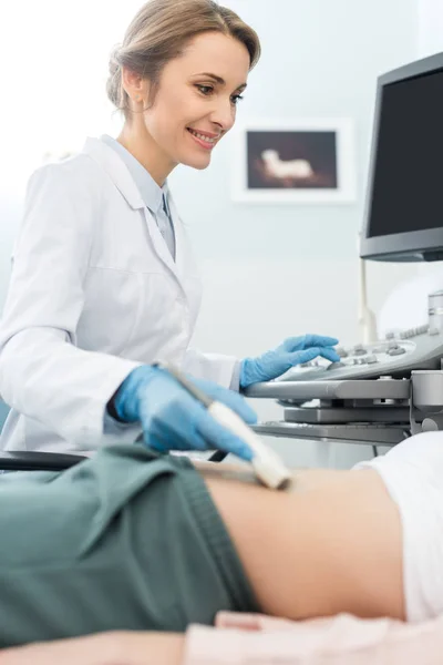 Sonriente médico examinando el estómago del paciente con ecografía en la clínica - foto de stock