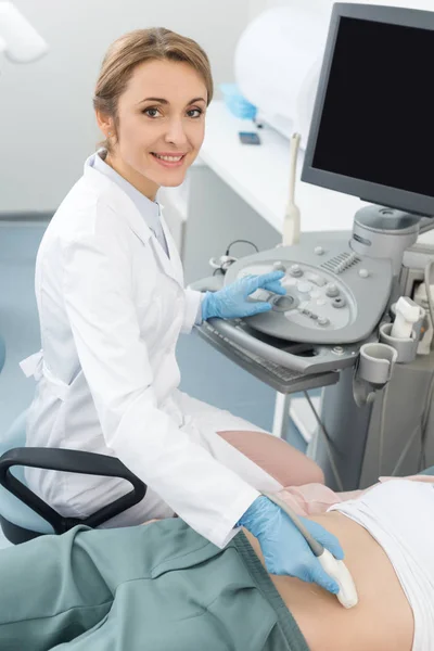 Médico sonriente examinando el estómago de una paciente con ecografía en la clínica - foto de stock