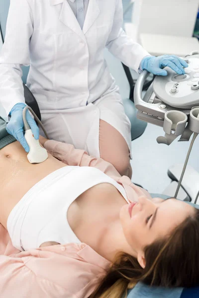 Female doctor examining stomach of young patient with ultrasound scan in clinic — Stock Photo