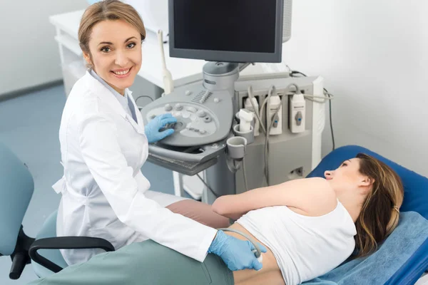 Улыбающийся врач, осматривающий почки пациентки с помощью ультразвукового сканирования в клинике — стоковое фото