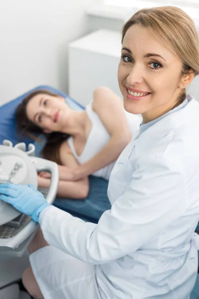 Médico sonriente examinando riñón de paciente femenina con ecografía en clínica - foto de stock