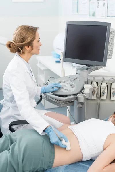 Médico profesional examinando el riñón de una paciente femenina con ecografía y mirando a la pantalla en blanco - foto de stock