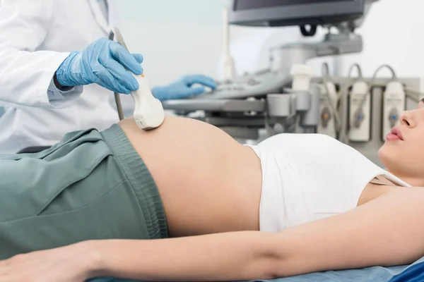 Vista recortada del médico examinando el vientre de la mujer embarazada con ecografía en la clínica - foto de stock