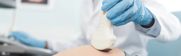 Panoramic shot of doctor examining belly of pregnant woman with ultrasound scan in clinic — Stock Photo