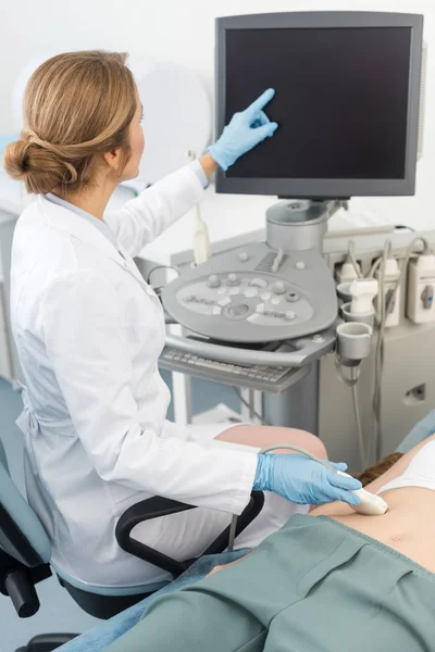 Blonde Ärztin macht Ultraschalluntersuchung des Magens und zeigt auf leeren Bildschirm — Stockfoto