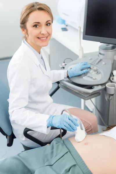 Médico sonriente examinando el vientre de la mujer embarazada con ecografía en la clínica - foto de stock