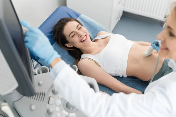 Doctor examining belly of happy pregnant woman with ultrasound scan in clinic — Stock Photo