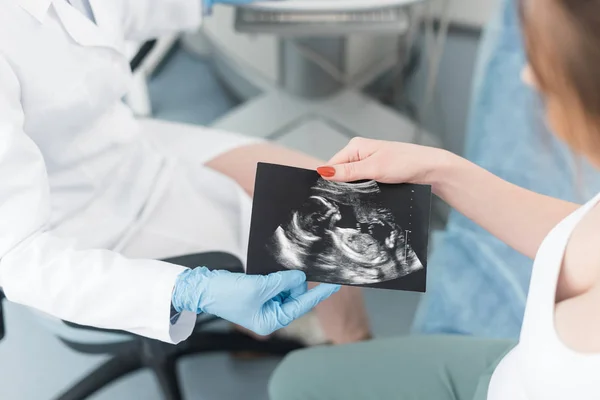 Vista ritagliata del medico che esegue la scansione a ultrasuoni a una giovane donna incinta in clinica — Foto stock
