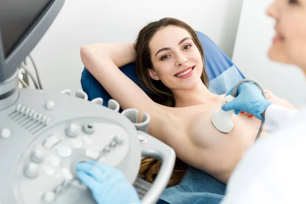 Vista recortada del médico haciendo el examen de mama para la paciente sonriente utilizando el escáner de ultrasonido - foto de stock