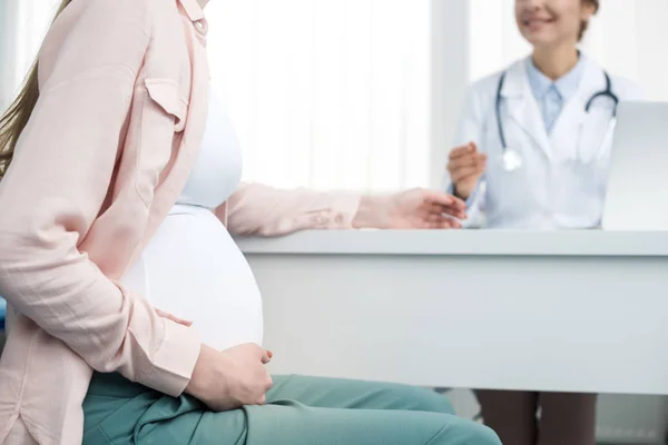 Vue recadrée de la jeune femme enceinte en consultation avec un gynécologue en clinique — Photo de stock