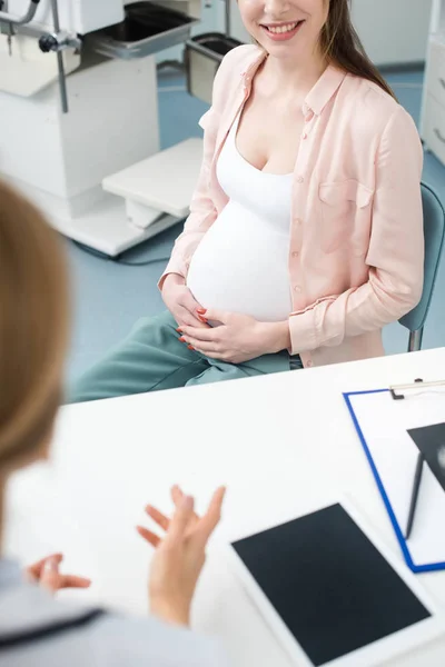 Ausgeschnittene Ansicht einer schwangeren Frau, die mit dem Frauenarzt in der Klinik Rücksprache hält — Stockfoto