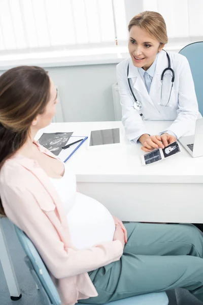 Красивый врач показывает ультразвук молодой беременной женщине в клинике — стоковое фото