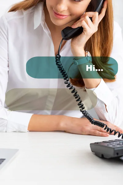 Vista recortada de una mujer de negocios sonriente hablando por teléfono cerca de la computadora portátil en la mesa, ilustración de diálogo - foto de stock