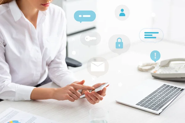 Cropped view of businesswoman using smartphone near document with chart and laptop on table, technology icons illustration — Stock Photo