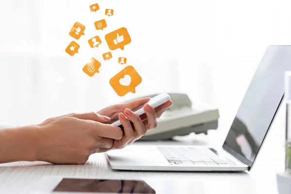 Cropped view of businesswoman using smartphone near digital tablet and laptop on table, social media illustration — Stock Photo