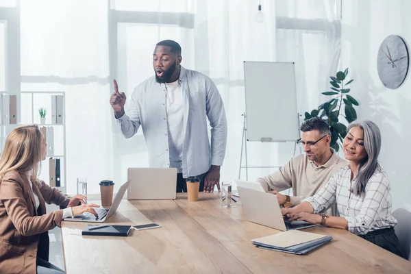 Afro-americano mostrando ideia e conversando com colegas durante reunião em agência criativa — Fotografia de Stock