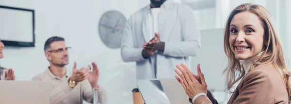 Colpo panoramico di donna sorridente applaudire con colleghi multiculturali — Foto stock