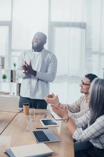 Smiling multicultural colleagues clapping during meeting in creative agency — Stock Photo